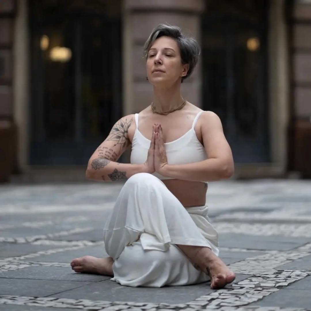 Praticante de cabelo curto sentada em meditação, de olhos fechados e mãos unidas diante do peito